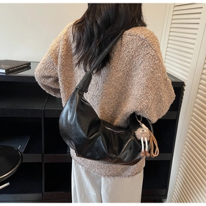 Close-up of black half-moon shoulder bag with sleek leather texture and plush charm