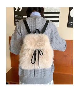 Close-up of beige plush backpack with black bow detail on a grey sweater
