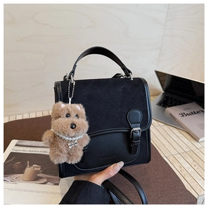 Detail of black crossbody bag with matte diamond quilting and plush dog keychain charm