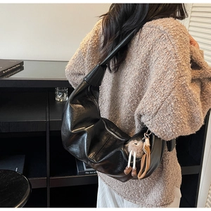 Detail of black glossy hobo bag with pleated texture and silver zipper on shoulder