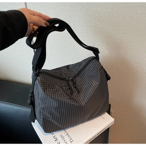 Detail of adjustable black nylon shoulder strap and dual zipper on plaid canvas bag