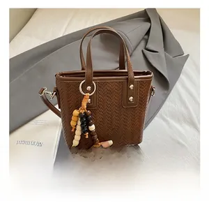 Détail de la texture tressée du sac seau marron et de son pendentif à pompon perlé