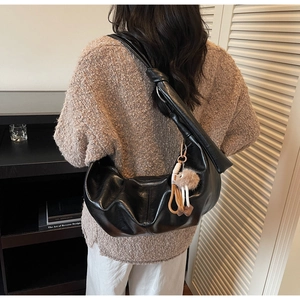 Detail of black large hobo bag featuring a knotted shoulder strap and plush charm decor