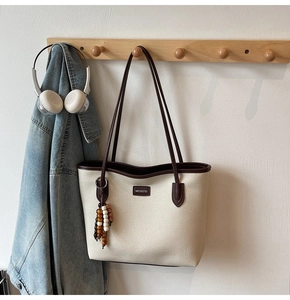 Detail einer beigen Canvas-Tasche mit braunem Lederbesatz und buntem Perlenanhänger