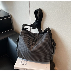 Detail of gray plaid canvas crossbody bag featuring wide nylon strap and plastic buckle