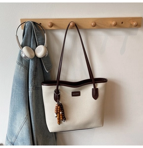 Close-up of canvas tote bag with brown leather trim and retro wooden bead tassel detail