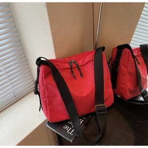 Detail of red checkered crossbody bag showing dual zippers and adjustable wide black strap