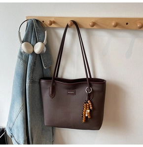 Deep brown tote bag with shoulder straps and beaded charm on a wooden coat rack
