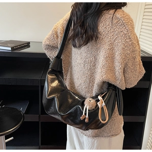 Model wearing black crescent shoulder bag with oily PU texture and plush ball charm decor