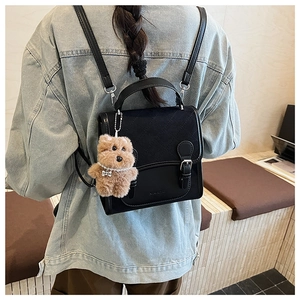 Close-up of black quilted mini backpack with a cute plush dog pendant on a model