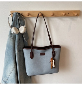 Detail of blue textured tote bag with brown leather straps hanging on a wooden hook
