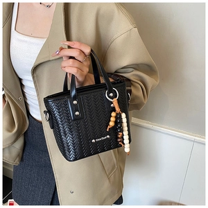 Gros plan détaillé du sac à main noir avec texture tressée, perles en bois et plaque argent