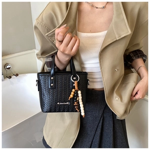 Détail d'un sac à main noir à texture tissée avec des breloques décoratives en perles