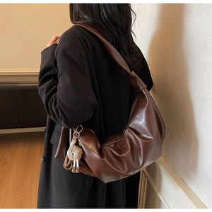 Brown leather hobo bag with knotted strap and cute bear pendant on a model shoulder