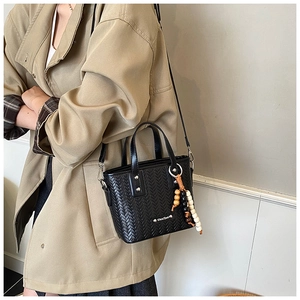 Détail du sac tissé noir avec breloque perlée porté avec un trench-coat kaki élégant