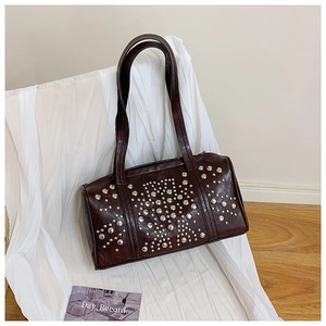 Detail of a dark brown studded barrel bag resting on white fabric in a bright room
