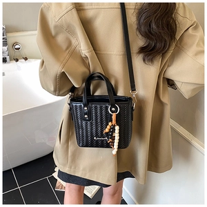 Détail d'un sac bandoulière tissé noir avec breloque perlée présenté sur un mannequin