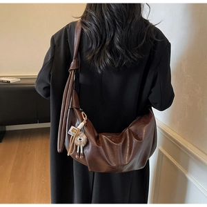 Detail of dark brown leather crescent bag with wide strap and plush doll pendant