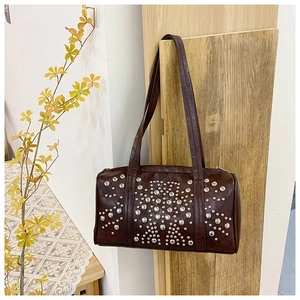 Detail of dark brown Boston bag with silver rivets and double shoulder straps on wood back