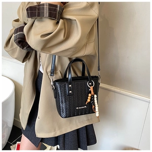 Détail d'un sac seau noir tressé avec pampille en bois et plaque logo métallique