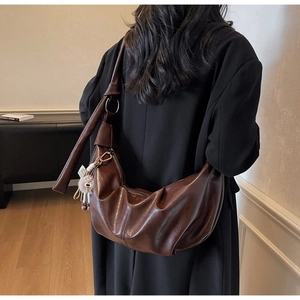 Detail of a brown glossy leather hobo bag featuring knotted straps and a plush cat charm