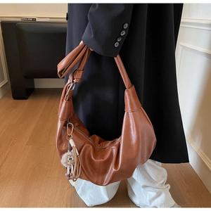 Detail of brown pleated hobo bag with knotted handle and decorative charm in lifestyle setting