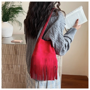 Close-up of red suede bucket bag with long tassels paired with a grey tweed knit sweater