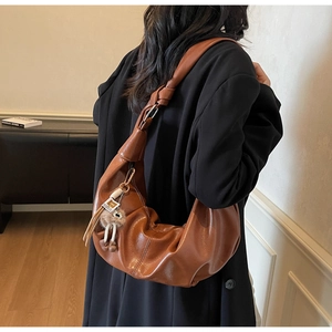 Detail of a brown leather crescent hobo bag with knotted strap and plush charm