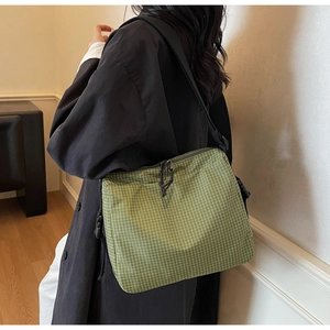 Detail of green checkered canvas messenger bag with adjustable strap and dual zippers