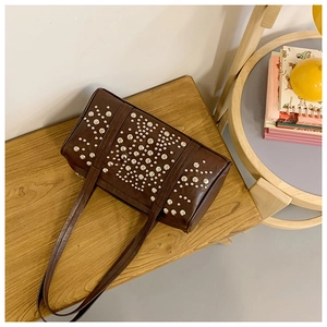 Close-up of deep brown cylinder bag featuring decorative silver rivets in a warm setting