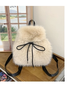 Close-up of beige faux fur backpack featuring a black drawstring bow on a wooden table