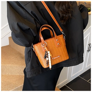 Détail du sac seau orange au design tissé avec breloque perlée et doubles poignées