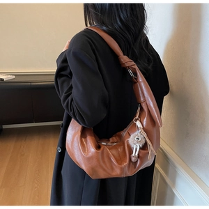 Close-up of brown crescent bag with large shoulder knot and cute pom-pom pendant charm