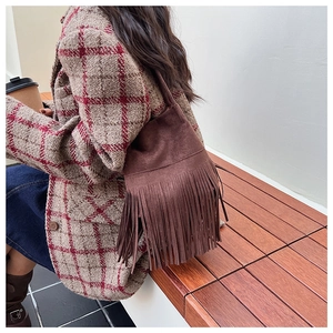 Detailed view of a dark brown suede bucket bag with long fringe tassels on a shoulder strap