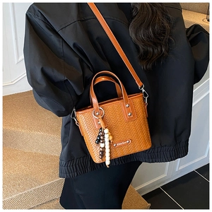 Détail du sac tressé marron avec rivets argentés et pendentif de perles colorées