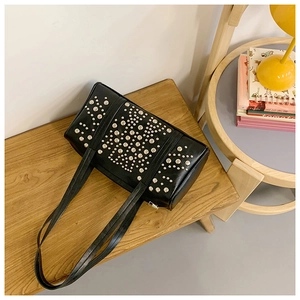 Close-up of black Boston bag with silver studs on a wooden surface with a lamp