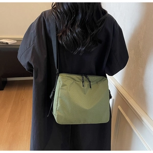 Detail of green plaid canvas crossbody bag featuring adjustable strap and secure zippers