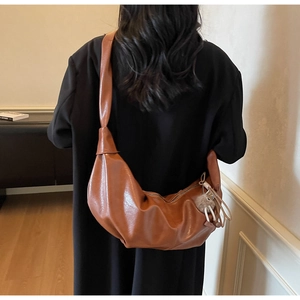 Detail of caramel crescent crossbody bag with decorative bear pendant and soft leather texture