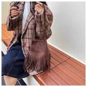 Close-up of brown suede bucket bag with long fringe tassels on a model outdoors