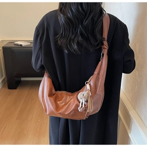 Rear view of brown crescent crossbody bag with plush charm on stylish shoulder strap
