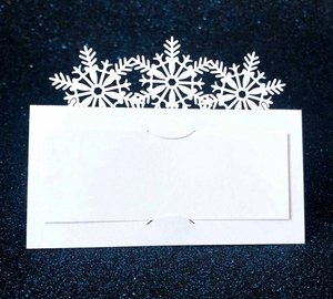 White laser-cut snowflake place cards for winter weddings on a navy blue glitter surface