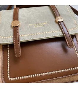 Close-up of green fabric and brown leather crossbody bag with gold logo and embroidery