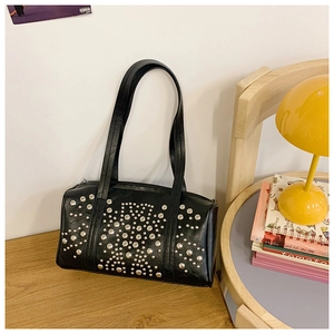 Detail of black rivet shoulder bag on a wooden table next to a stylish mushroom lamp