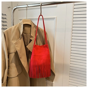 Detail of red faux suede bucket bag with long fringe tassels hanging in a boutique setting