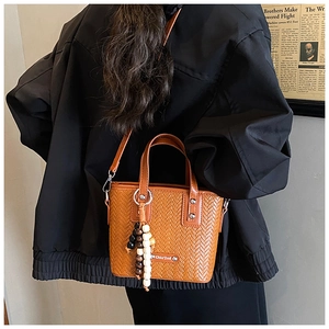 Sac fourre-tout tressé marron caramel avec breloque porté par un mannequin chic