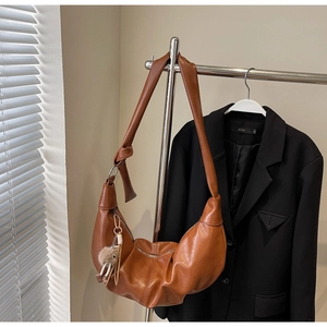 Detail of caramel half-moon crossbody bag with soft faux leather texture and fur ball charm