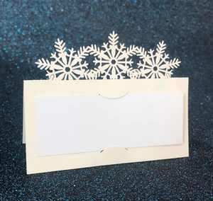 Laser cut white snowflake place cards for Christmas weddings on blue glitter background