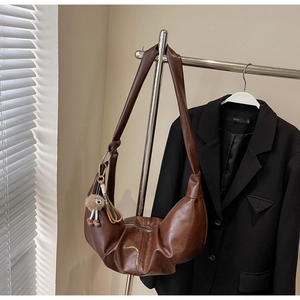 Detail of dark brown leather crescent bag featuring a cute plush pendant on a metal rack