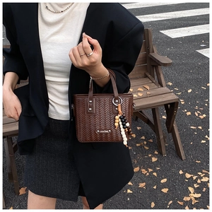 Détail d'un sac bandoulière tressé marron avec logo Chla'zod et charm en perles de bois