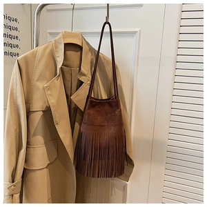Detail of dark brown suede bucket bag with long fringe accents beside a khaki trench coat
